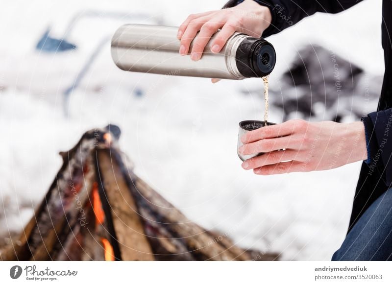 Reisende Hände Mann Nahaufnahme gießt Tee aus Fläschchen in eine Tasse im Wald in der Nähe eines Lagerfeuers. Abenteuer Herbst Camping Kaffee trinken Flasche