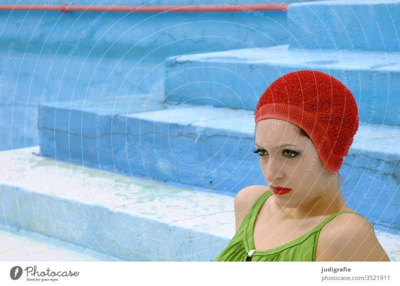 Das Mädchen mit der schönen roten Badekappe und grünem Badeanzug sitzt auf der Treppe des leeren Nichtschwimmerbeckens. Eine Sommerliebe. Frau Badebekleidung