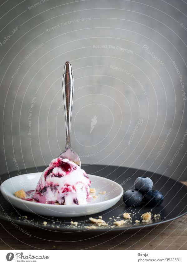 Eine Kugel Heidelbeereis mit einem Löffel auf einem Teller, rustikaler Stil Speiseeis kugel gefroren Sommer Dessert süß Geldautomat grau servierfertig