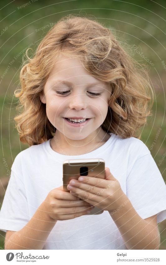 Lustiges Kind mit langen Haaren, das ein Handy hält. Telefon Park Freizeit Funktelefon Kindheit Smartphone Lifestyle Junge blond Mitteilung Anschluss