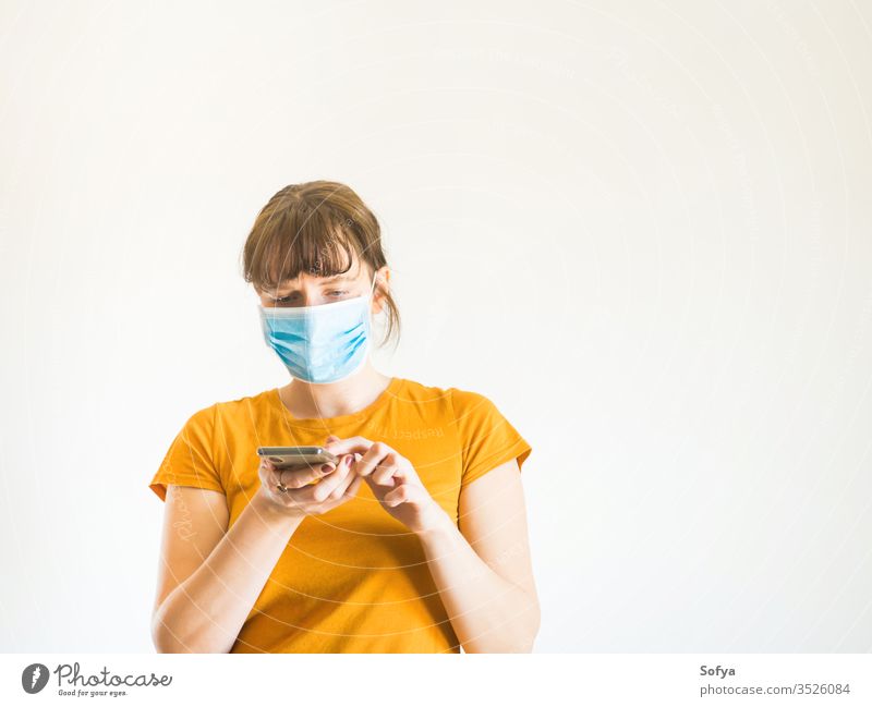 Junge Frau mit Gesichtsmaske und Smartphone Mundschutz COVID19 benutzend Mobile Telefon digital Anruf Hotline Helpline abstützen Coronavirus Person Quarantäne