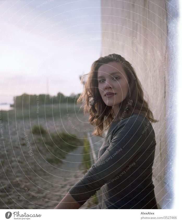 analoges Portrait mit Lichterscheinung einer jungen Frau im Kleid vor einer Wand Mädchen schön groß sportlich schlank fit brünett Locken langes Haar Beton Sand