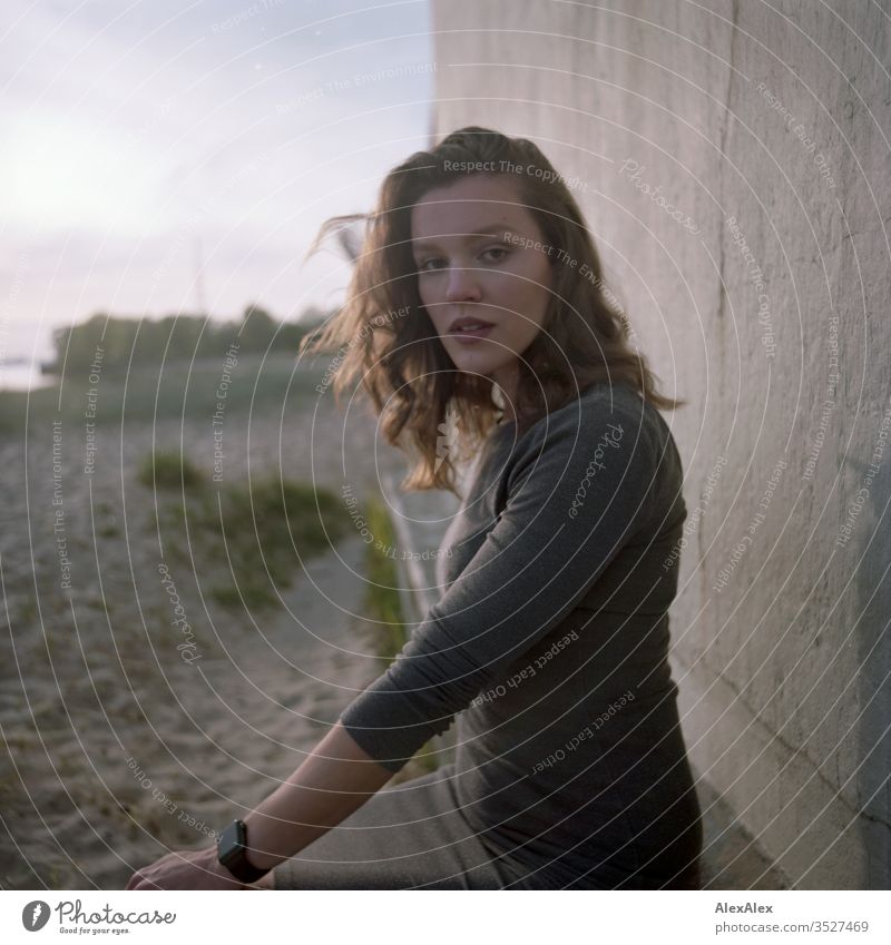 analoges Portrait einer jungen Frau im Kleid vor einer Wand Mädchen schön groß sportlich schlank fit brünett Locken langes Haar Beton Sand Strand Abend Körnung