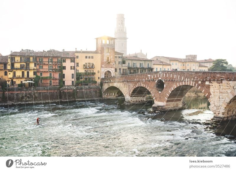 Flusssurfer bei Sonnenuntergang mit Blick auf die Stadt bei Ponte Pietra in Verona, Italien Surfer Sport Italienisch Turm Gebäude ponte pietra Brücke Europa