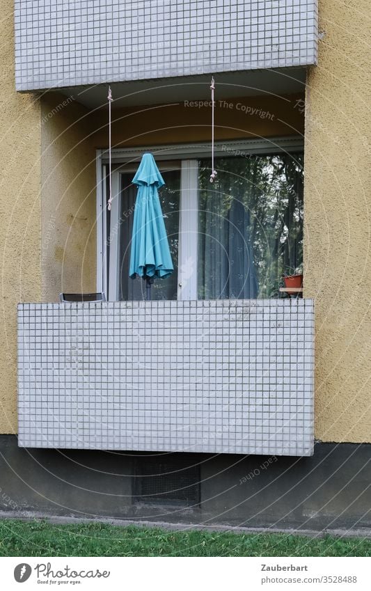 Balkon einer Wohnung in einem Wohnhaus der 60er Jahre mit hellblauem Sonnenschirm Erdgeschoss Fliesen Kacheln Muster gelb zuhause bescheiden Fenster