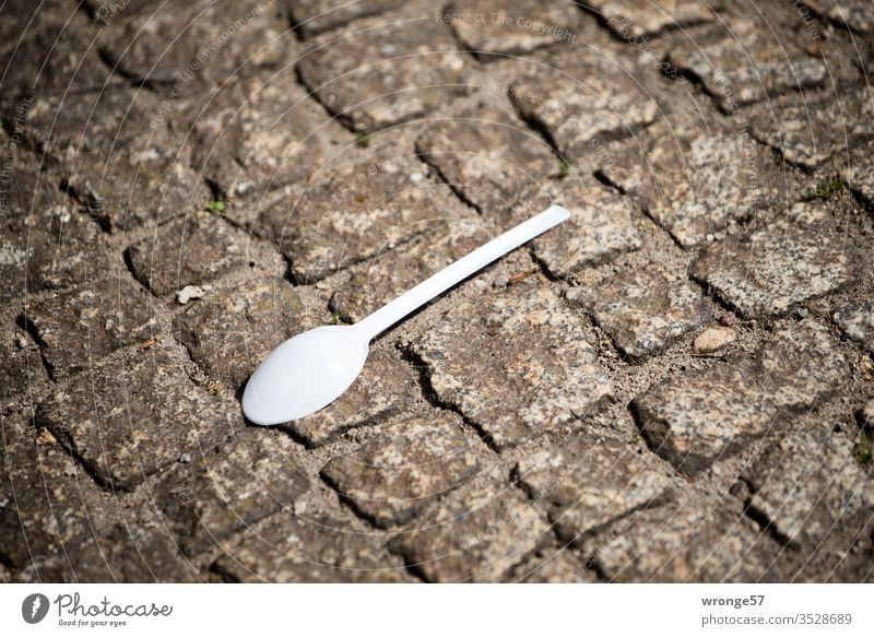 Plastiklöffel liegt auf dem Gehweg herum Löffel Besteck Ernährung Straße Pflastersteine Farbfoto Gedeckte Farben weiß braun verloren verloren gegangen