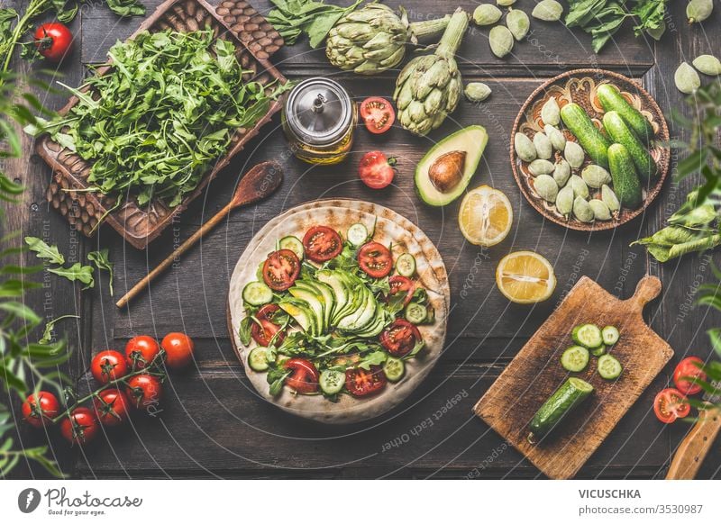 Gesunde vegetarische Zutaten für das Mittagessen. Tortilla umhüllt mit frischem Gemüse, Avocado, Olivenöl und Zitrone auf rustikalem Holzküchentisch, von oben gesehen. Vorbereitung zum Kochen. Veganes Essen.