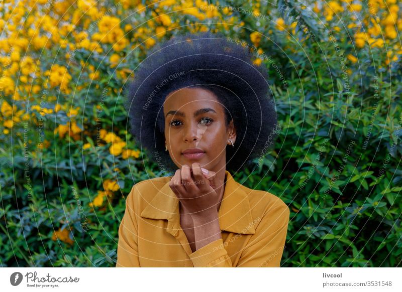 junge Frau mit Afro-Haaren in einem Garten mit gelben Blumen schwarze Frau Mädchen Menschen Porträt Lifestyle cool lieblich gelbe Blume im Freien Außenseite