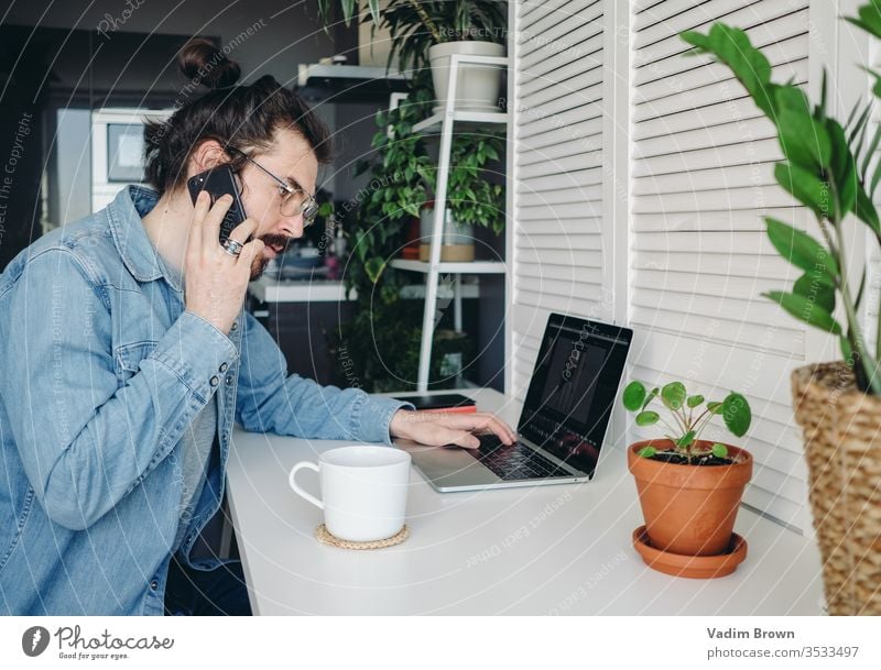 Junger Mann mit Bart sitzt auf dem Stuhl und benutzt einen Laptop. Freiberufliche Arbeit von zu Hause im Quarantänekonzept Video-Chat Online-Shopping