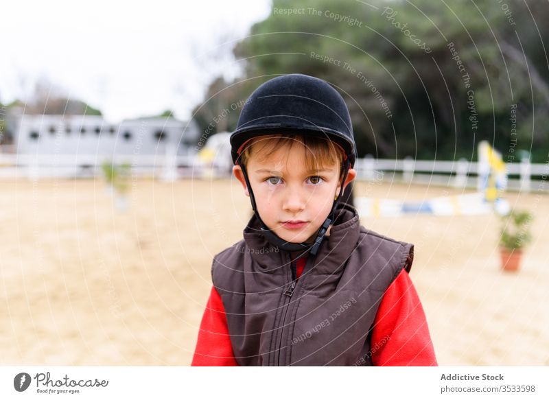 Kleiner Junge auf dem Dressurviereck Jockey Sattelkammer Training Reiterin Schule Arena Schutzhelm Männerweste Kind wenig niedlich bezaubernd Sport Tracht