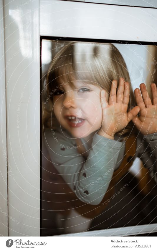 Glückliches kleines Mädchen hinter dem Fenster heimwärts Lächeln lässig niedlich wenig berühren Glas Kind heiter Kindheit Raum spielerisch neugierig ruhen