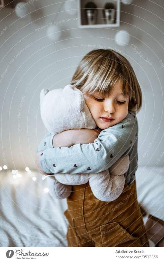 Glückliches Mädchen spielt auf weichem Bett spielen Spielzeug Umarmung Lachen Lichterkette Plüsch Lügen aufgeregt Kind Liebe Girlande Schlafzimmer wenig