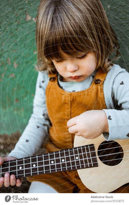 Mädchen mit Ukulele an schäbiger Wand sitzend Musik Kickroller spielen lässig wenig rau Boden verwittert grün Kind Straße Gebäude Grunge Instrument Klang Talent