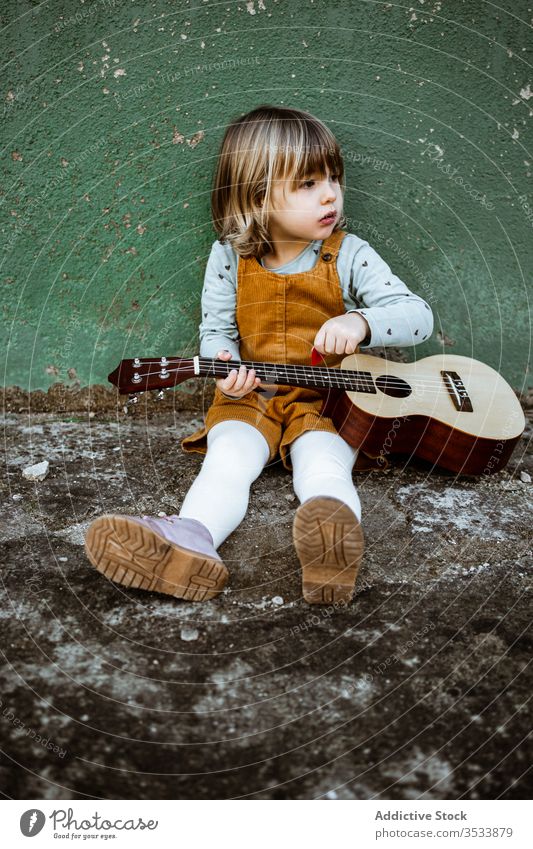 Mädchen mit Ukulele an schäbiger Wand sitzend Musik Kickroller spielen lässig wenig rau Boden verwittert grün Kind Straße Gebäude Grunge Instrument Klang Talent