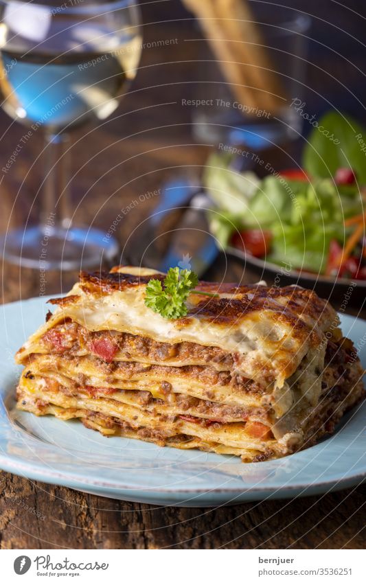 Portion frischer Lasagne auf einem Teller Abend grissini Sommer Wein weiß Holz rustikal Salat Fleisch Hackfleisch Scheibe lecker Kräuter bolognese bolognaise