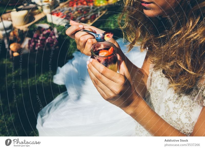 Anonyme junge Frau in weißem Brautkleid isst Beerendessert im Garten Dessert Sommer Frucht feiern elegant frisch süß Party Hochzeit Kleid Mittagessen Löffel