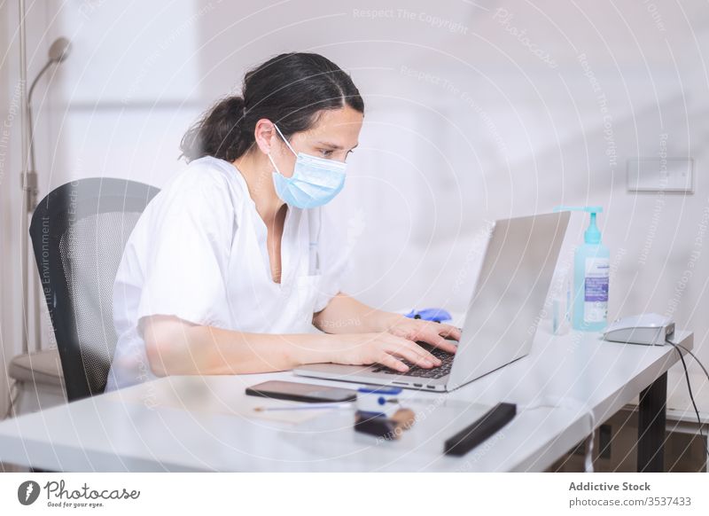 Junge Ärztin mit medizinischer Maske arbeitet am Laptop in der Klinik Frau Arzt Uniform Mundschutz Handschuh Schreibtisch ernst Krankenhaus professionell