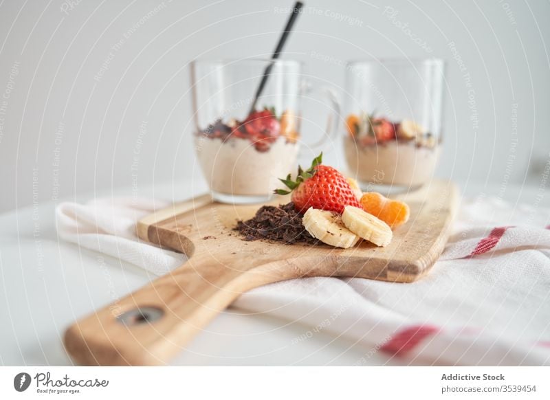 Becher Joghurt mit Früchten Frucht Tasse Frühstück Morgen Dessert Erdbeeren Mandarine Banane Schokolade frisch lecker Glas Schneidebrett hölzern Lebensmittel