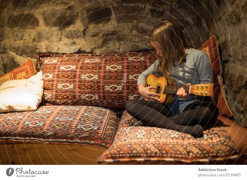 Ukulele spielendes Mädchen auf der Couch in einem Steinhaus während eines Urlaubs in Spanien Liege Haus Land üben Sofa Musik Komfort gemütlich Kantabrien