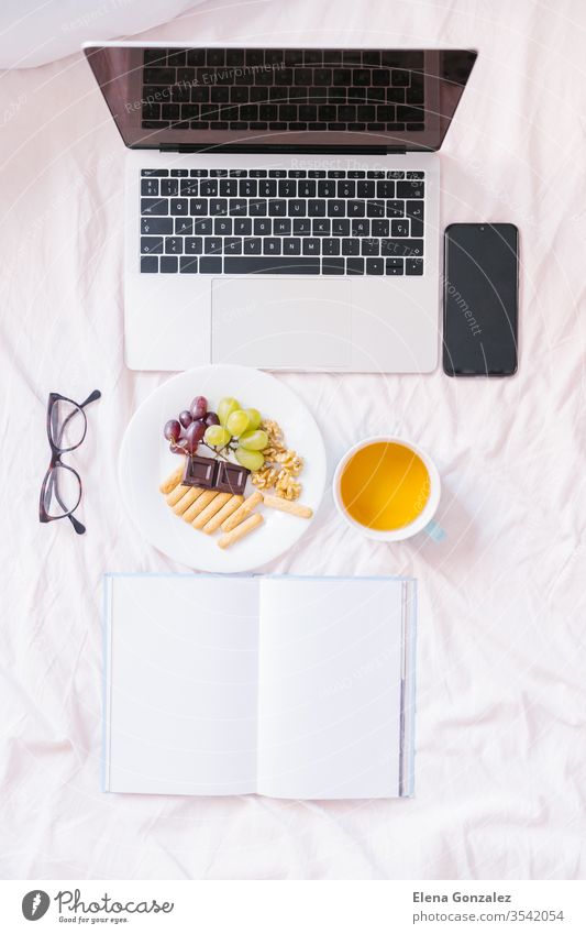 Flacher Schlag. Zu Hause im Bett Tee trinken, ihren Laptop überprüfen, ein Buch lesen und frühstücken. Ansicht von oben flache Verlegung Bücher Frühstück Snack