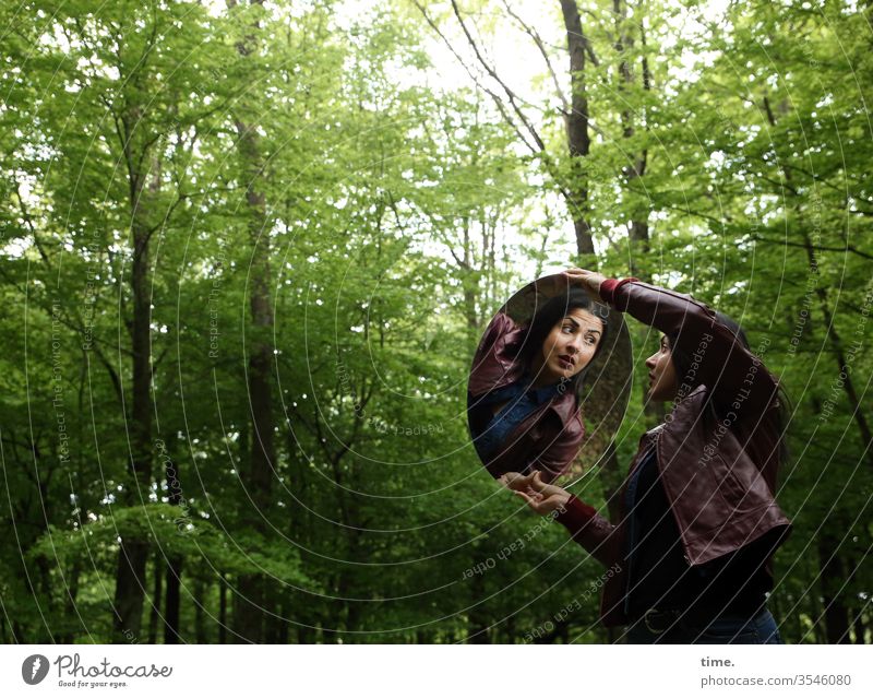 Estila frau feminin wald schauen beobachten dunkel grün wild langhaarig dunkelhaarig lederjacke spiegel halten erstaunt laubwald