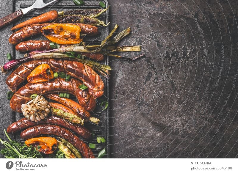 Dunkler Braten im Hintergrund mit gegrillten Würstchen und gebratenem Gemüse. Ansicht von oben. Barbecue-Grill-Partyplatte. dunkel Lebensmittelhintergrund