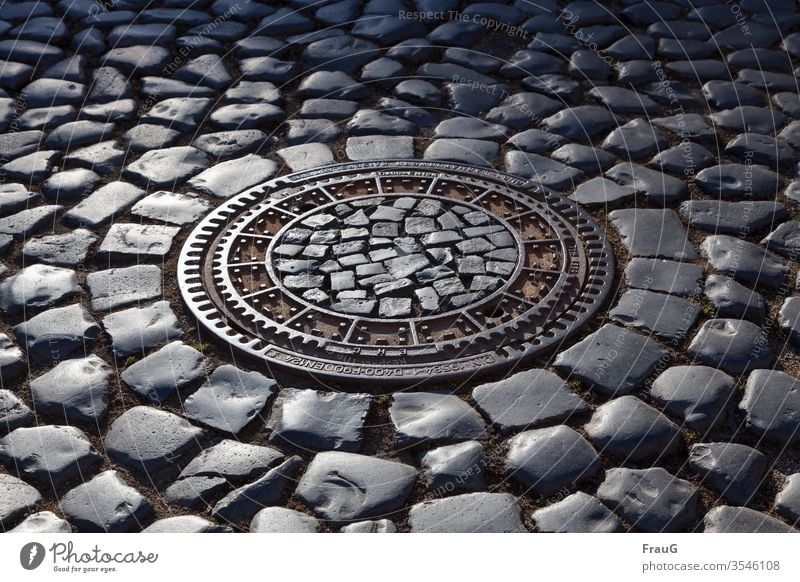 Gullideckel im Kopfsteinpflaster bei Abendlicht Altstadt Straße Kanalisation gepflasterte Straße Pflastersteine Gullydeckel Natursteinpflaster Katzenköpfe Stadt