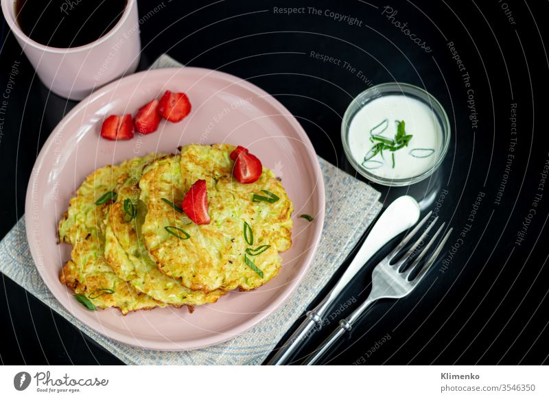 Zucchinikrapfen, vegetarische Zucchinikrapfen, serviert mit frischen Kräutern und saurer Sahne. Garniert mit Erdbeeren und grünen Zwiebeln. Auf dunklem Hintergrund.