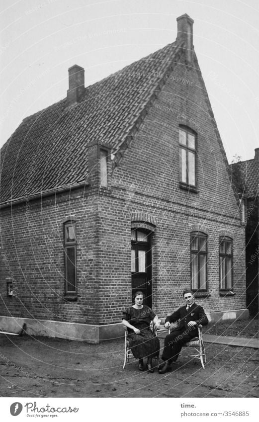 Stolz vor der Hütte mann frau nostalgie sitzen zusammen gemeinsam festlich anzug ernst skeptisch damals früher paar haus stolz heim backstein sessel stuhl