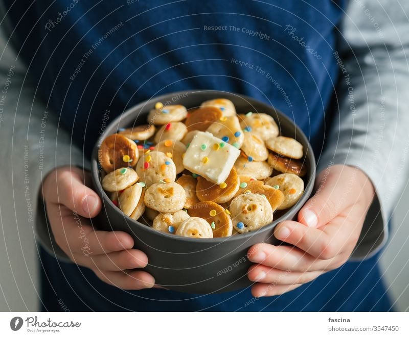 Pfannkuchenmüsli in Babyhänden, Kopierfeld Pfannkuchen-Getreide winzige Pfannkuchen Mini-Pfannkuchen Kind Müsli Hände Textfreiraum Halt Nahaufnahme Streusel