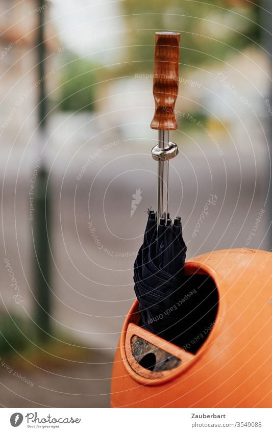 Schwarzer Regenschirm mit Holzgriff steckt in orangefarbener Mülltonne schwarz Griff stecken Sonne Schwache Tiefenschärfe oval Berlin BSR Straße Abfall