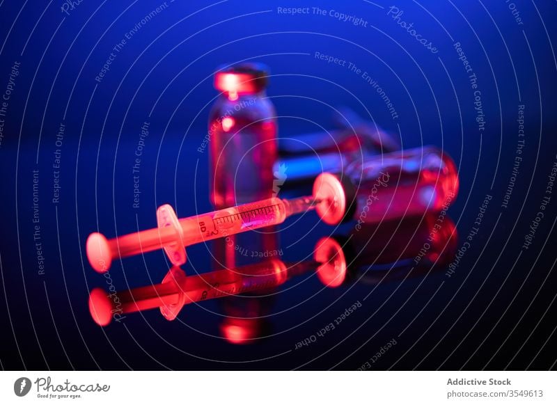 Spritze mit Nadel im dunklen Raum in der Kappe der Flasche Impfstoff Medikament Kur Bund 19 Infektion Virus Coronavirus neonfarbig leuchten durchsichtig