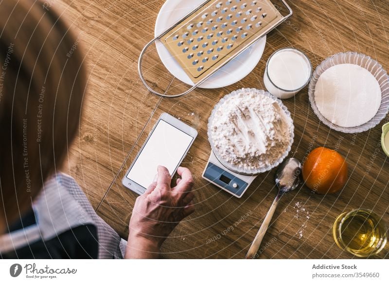 Frau benutzt Mobiltelefon während der Zubereitung von Gebäck Bestandteil backen Smartphone Skala Browsen Gewicht Teigwaren Küche vorbereiten Koch Hand Rezept