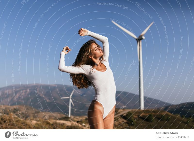 Zarte Frau tanzt allein in der Nähe des Windparks auf sonnigem Feld Tanzen Landschaft sinnlich Natur Ökologie schlank Stil hochreichen alternativ Windmühle