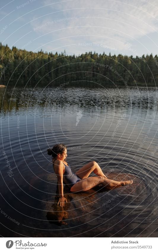 Frau im Badeanzug sitzt im See Wasser Windstille Sonnenuntergang genießen Sommer majestätisch sitzen Landschaft Wald ruhig Gelassenheit Harmonie friedlich