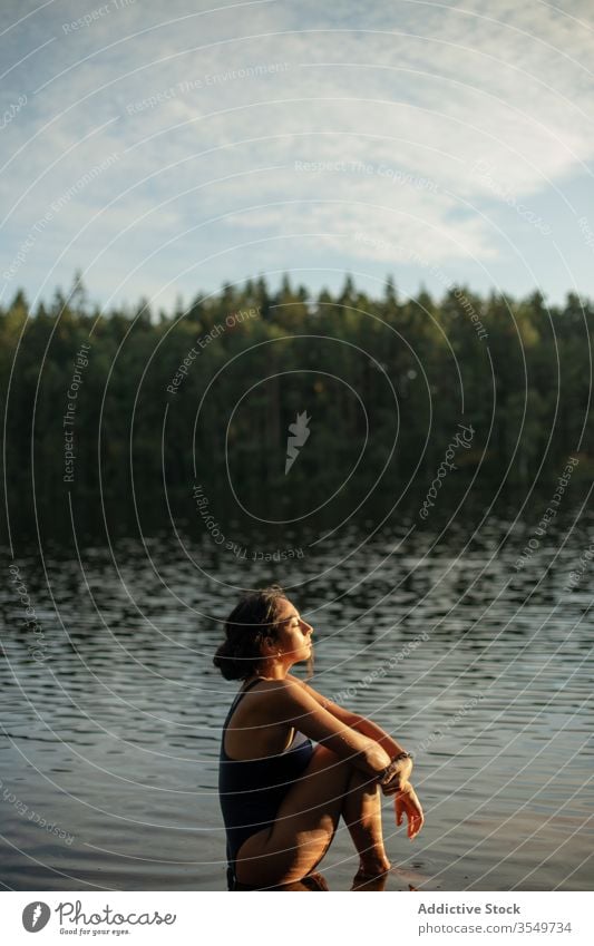 Frau im Badeanzug sitzt im See Wasser Windstille Sonnenuntergang genießen Sommer majestätisch sitzen Landschaft Wald ruhig Gelassenheit Harmonie friedlich