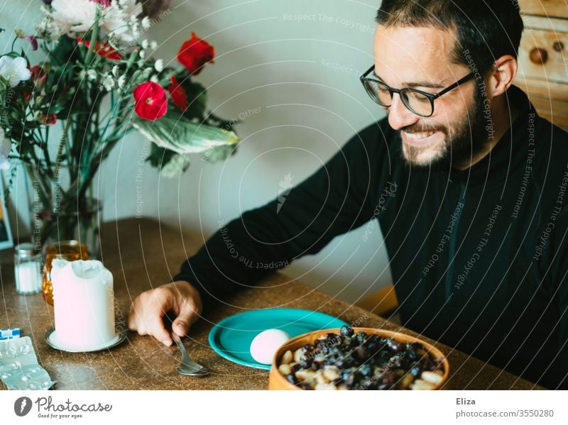 Ein Mann sitzt am Tisch beim Essen und lacht weil er gute Laune hat sitzen lachen gemütlich Frühstück Lächeln froh fröhlich Esstisch zuhause stayhome