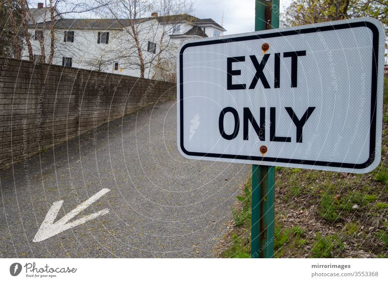 Vorstadtgebiet mit Ausfahrtsstraße mit aufgemaltem Pfeil auf dem Asphalt und grünem Pfahl schwarz-weißes Schild mit der Aufschrift "Exit Only".