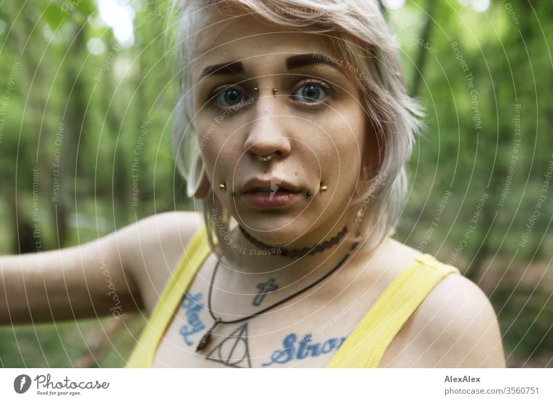 Portrait einer jungen Frau mit Piercings, Tätowierungen und Tunnel Mädchen blond Schmuck Assecoires Schulter Shirt Hemd schön draussen schauen beaobachten gelb