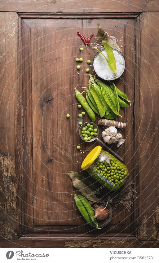 Frische Gartenerbsen in Dosen im Glas mit Gewürzen auf einem rustikalen Holztisch, Draufsicht. Einmachen der Gemüseernte. Erbsen Konservenherstellung Vegetarier