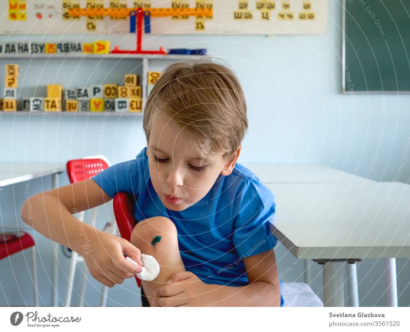 Ein Junge mit einem gebrochenen Knie schlägt auf die Wunde. Verletzte Kinder, Krankenversicherung, Erste Hilfe, Kinderbetreuung, Konzept des Erwachsenwerdens.