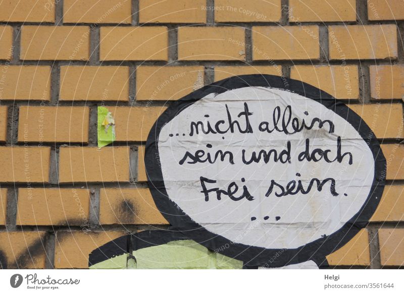 nicht allein sein und doch frei sein - geschrieben in schwarzer Schrift auf weißem Grund in Sprechblase an einer Klinkerwand Spruch Wunsch Wand Außenaufnahme