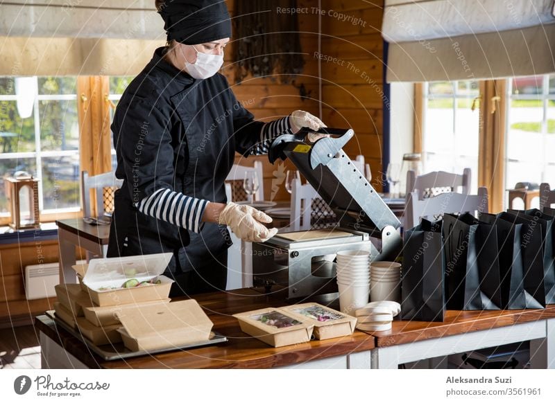 Restaurantmitarbeiter mit Schutzmaske und Handschuhen, die in Lebensmittelkartons verpacktes Essen zum Mitnehmen verpacken. Lebensmittellieferdienste und kontaktloser Online-Einkauf von Lebensmitteln.