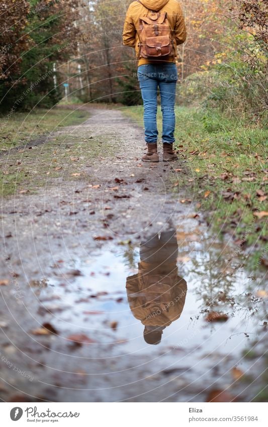 Mann steht auf einem Weg im Wald und spiegelt sich in einer Pfütze Spiegelung Spaziergang Regen Matsch Herbst Ausflug Wanderung wandern Reflexion & Spiegelung