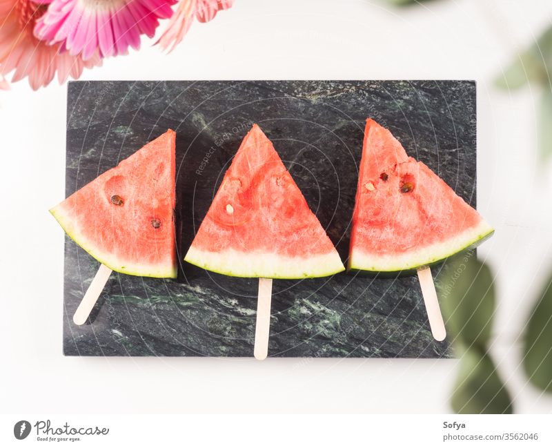 Wassermelonenscheibe Eis am Stiel auf Marmortablett Stieleis Sommer Scheiben Murmel rosa Tablett weiß hölzern Tisch frisch Snack Beeren Blumen lecker schön hell