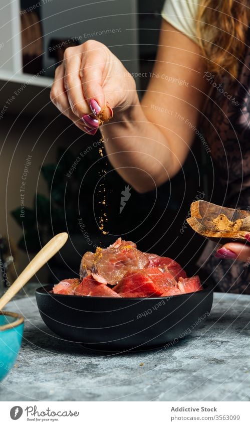 Weibliche Köchin beim Pökeln von Fleischstücken in der Küche Salz hinzufügen Frau Rindfleisch Schalen & Schüsseln roh Scheibe vorbereiten Koch Schürze Hausfrau