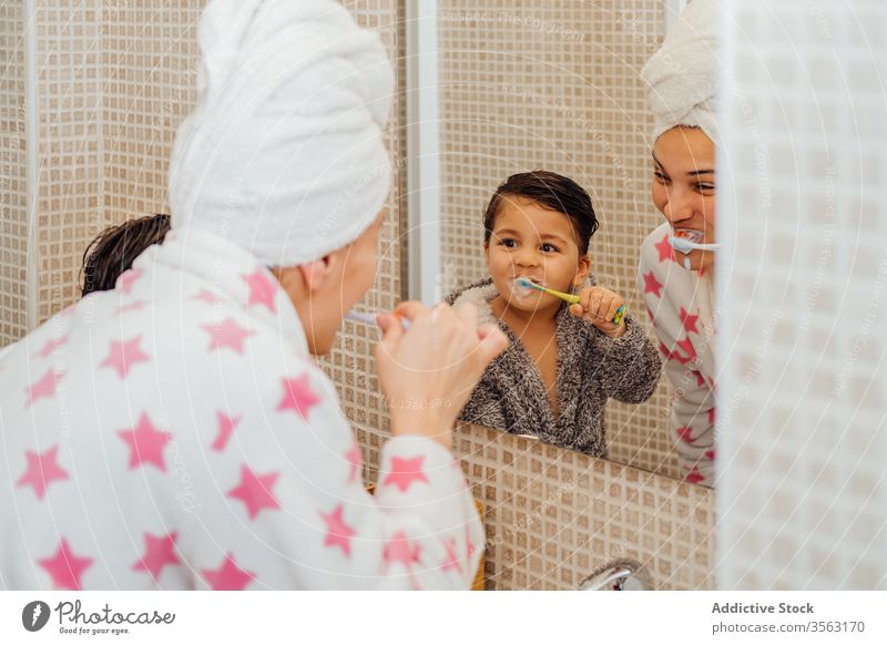 Fröhlicher Sohn und Mutter mit Zahnbürste im Badezimmer Bürste Zähne Junge Bademantel mündlich Hygiene Lächeln wenig Kind Mama Elternschaft Gesundheit Spiegel