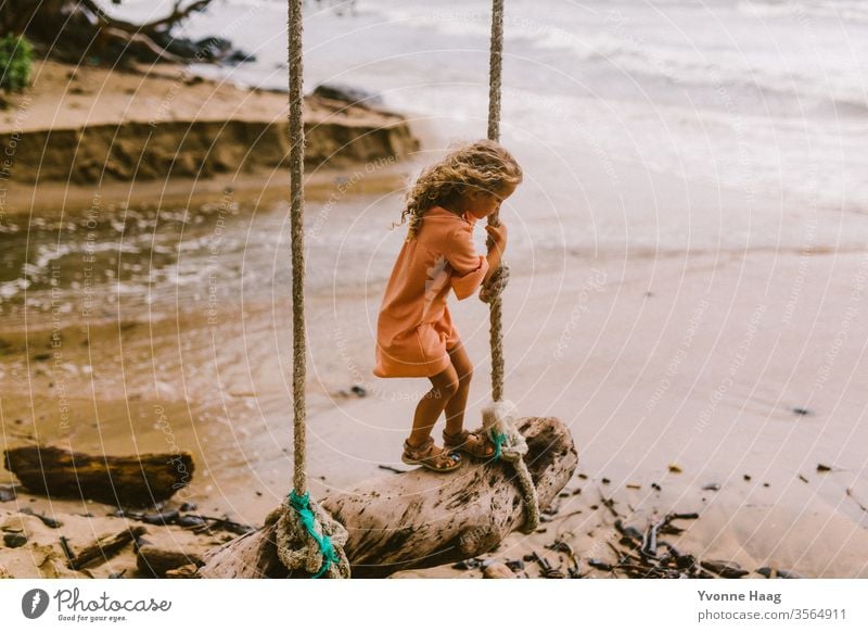 Mädchen steht auf einer Schaukel und schaukelt dem Meer entgegen Hawaii Hawaiiblume schaukeln Schaukelnd Freude Spielen Außenaufnahme Farbfoto Spielplatz