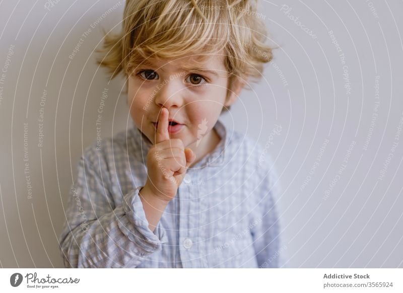 Anbetungswürdiger Junge mit Schweigegeste Stille gestikulieren bezaubernd Zeigefinger wenig niedlich Kind Inhalt Kindheit lässig Gesichtsausdruck Glück stehen