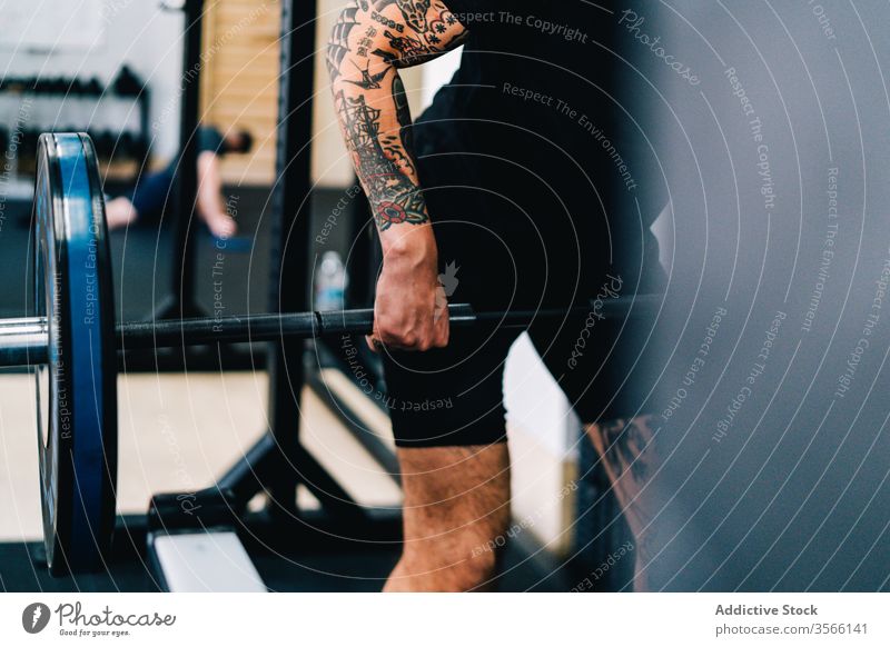 Kräftiger männlicher Athlet beim Training mit Langhantel Curl-Hantel Übung Sportler Totlift üben Tattoo Fitnessstudio Gerät brutal modern Metall T-Shirt Shorts